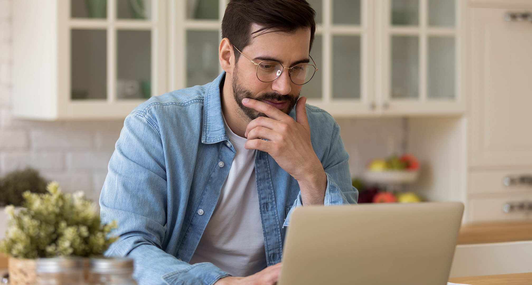 osoba s okuliarmi sediaca v kuchyni a pozerajúca sa na notebook